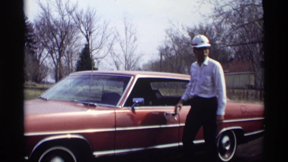 The hard-hatted man stands outside the closed reddish-brown sedan in the Savage, Minnesota home-movie footage from 1969.