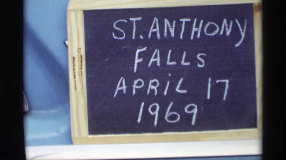 A handheld chalkboard slate records St. Anthony Falls, April 17, 1969, against a car-like background.