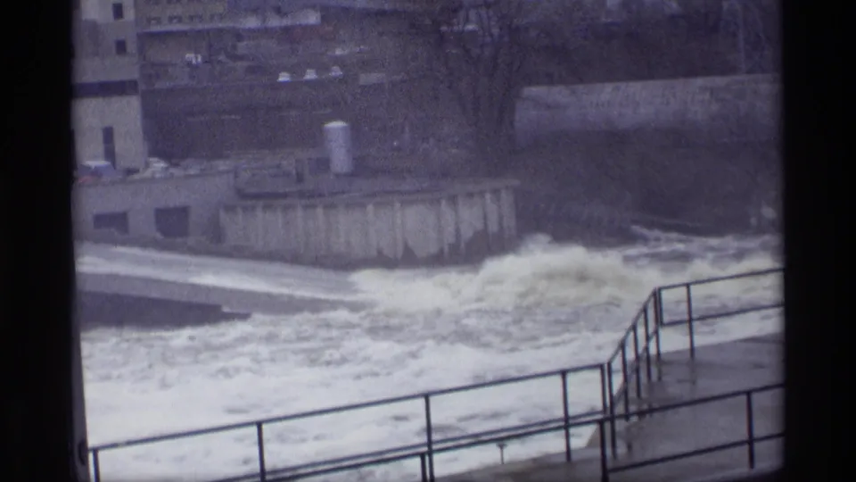 Later frame shifts to a side angle on the Savage dam outflow, showing concrete walls, railings, spray, and turbulent water below.