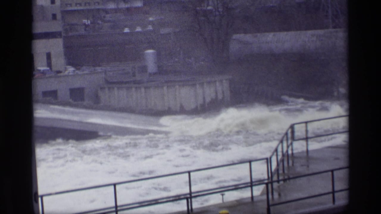 Turbulent river water rushing past a concrete spillway with railings in the foreground.