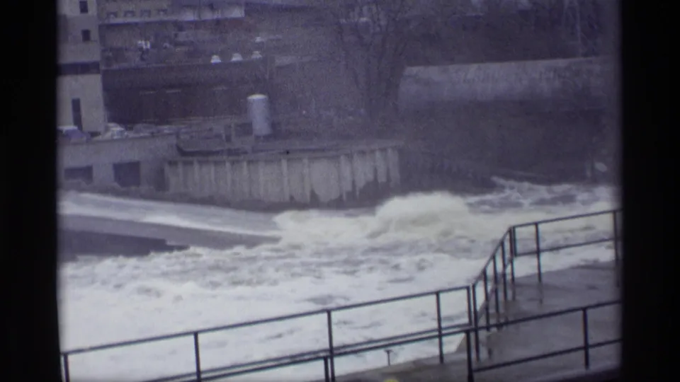 Savage, Minnesota 1969 home-movie frame showing whitewater surging past a concrete dam and foreground railings.