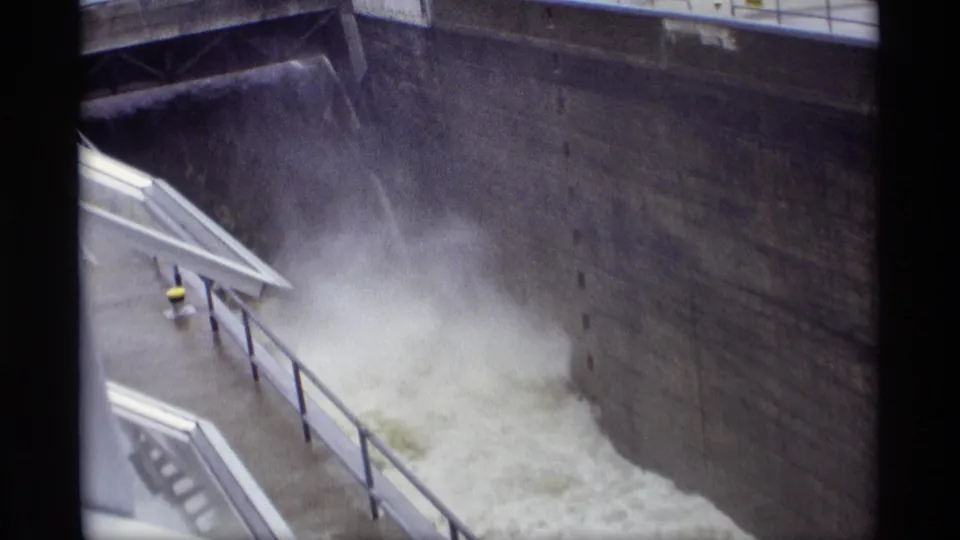 1969 8mm frame from Savage, Minnesota showing forceful water in a concrete channel below a railed walkway.
