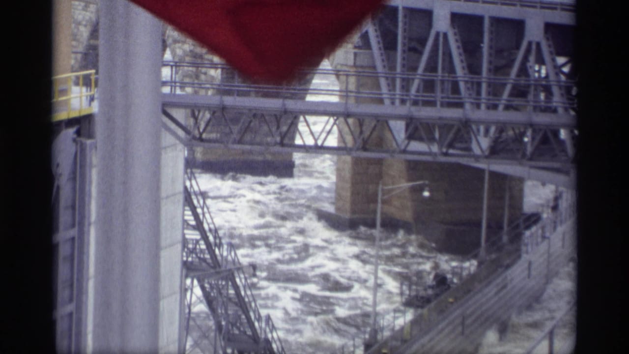 1969 8mm view in Savage, Minnesota, showing turbulent river water under steel and concrete bridge structures.
