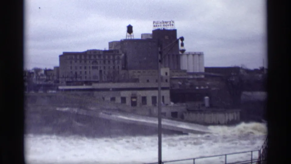 Savage, Minnesota riverfront view with churning water, industrial buildings, a water tower, and a visible Pillsbury's sign.
