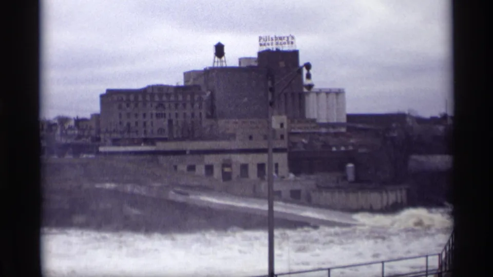 Savage, Minnesota 8mm frame showing industrial riverbank buildings, a Pillsbury's sign, and rough water under an overcast sky.