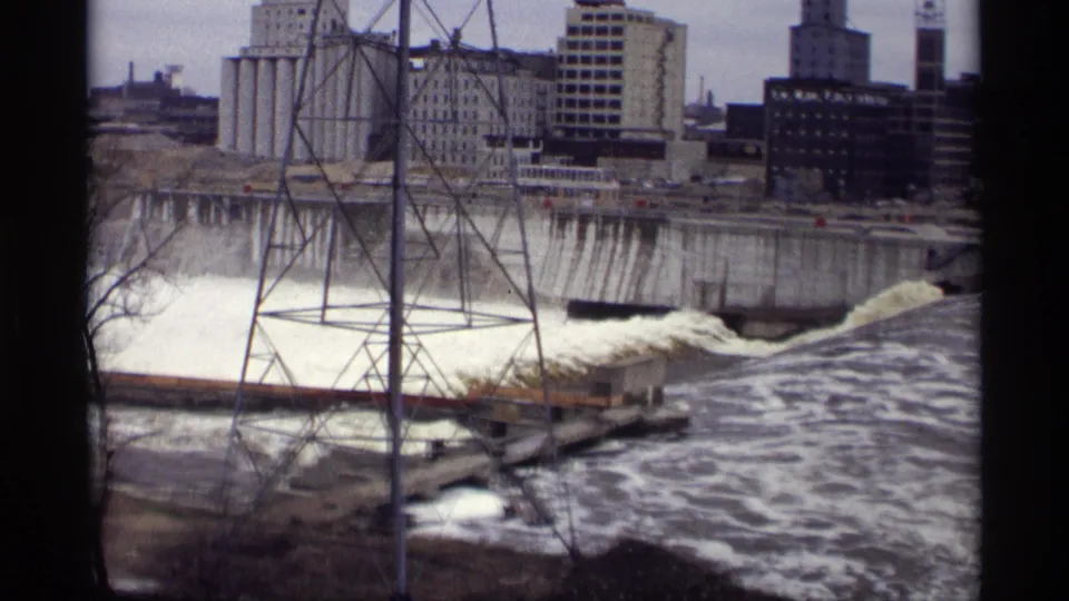 Savage, Minnesota industrial river scene from 1969, with rough downstream water, a dam edge, tower structure, and large buildings.