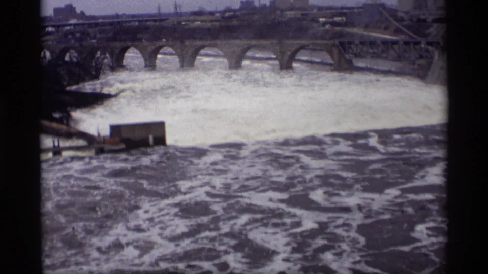 1969 Savage, Minnesota 8mm frame with churning river water below and a multi-arched bridge crossing the far side.