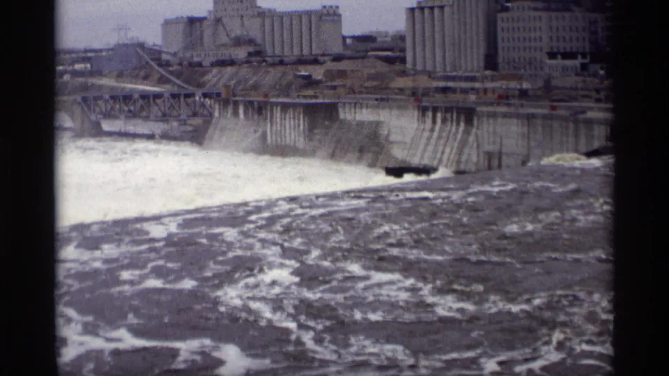 1969 Savage, Minnesota footage showing a wide view of rapids below a dam with grain elevators and industrial structures across the river.