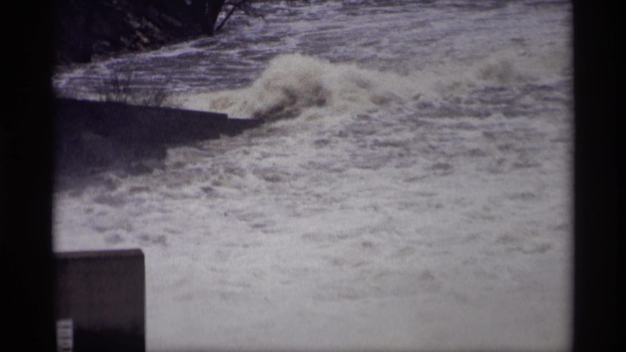 1969 Savage, Minnesota 8mm frame showing whitewater surging near a concrete riverside structure and dark tree line.