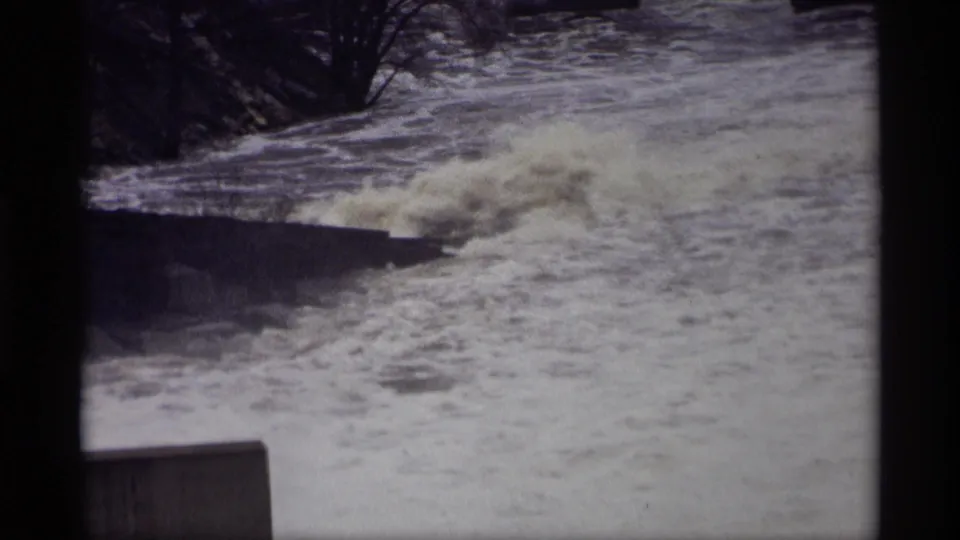 1969 Savage, Minnesota home-movie frame showing choppy water, spray, and a dark concrete edge along the river.
