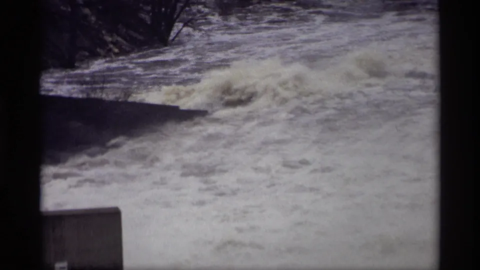 1969 Savage, Minnesota 8mm frame showing a broad foaming surge of river water near trees and a concrete edge.