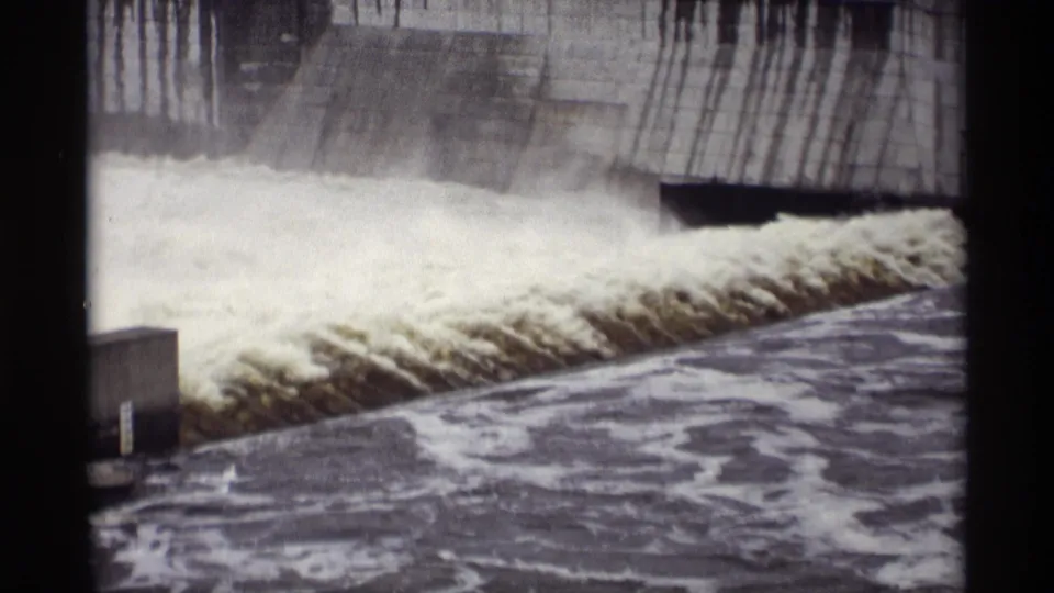 1969 8mm view of a concrete dam structure in Savage, Minnesota with foamy runoff surging from the spillway area.