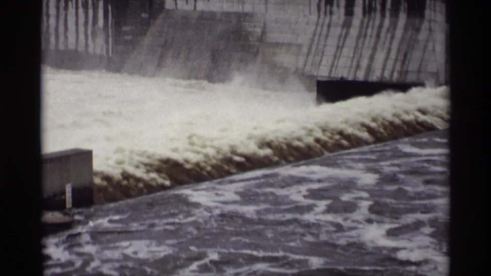 1969 Minnesota 8mm frame showing turbulent water rushing over a concrete spillway at a hydroelectric site.