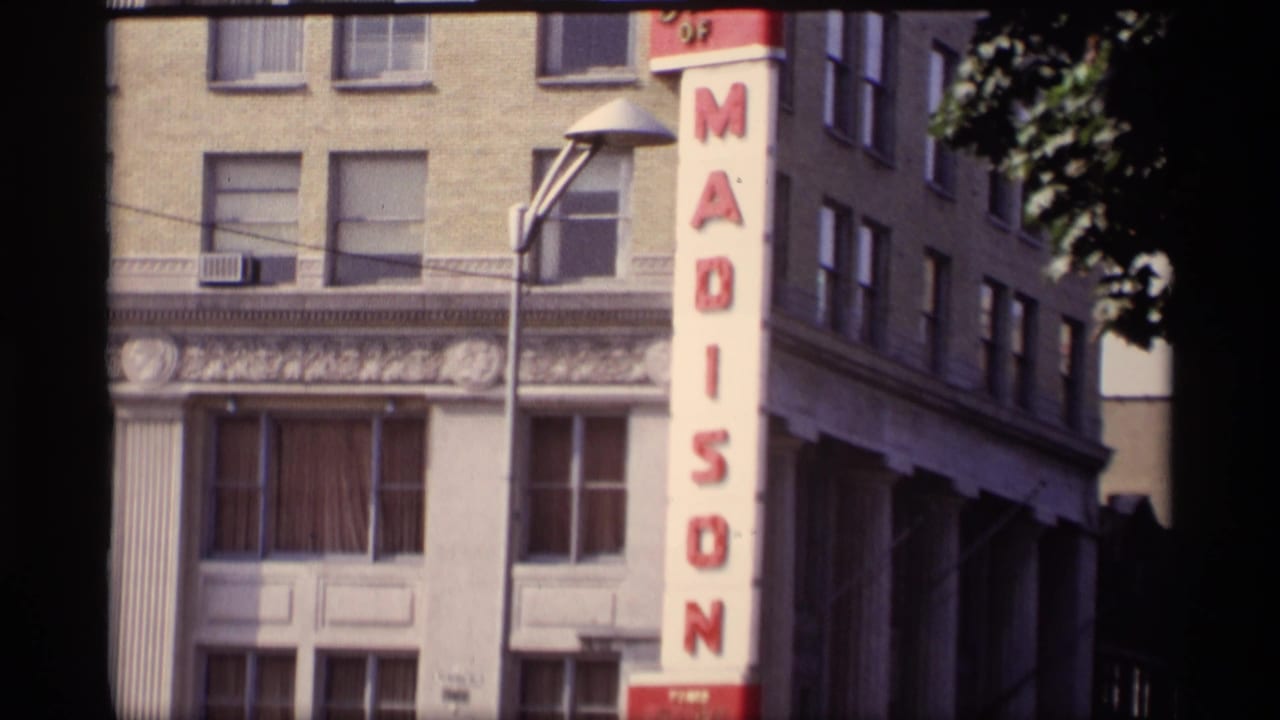 1969 Wisconsin 8mm frame showing a vertical Madison sign, masonry building facade, windows, and a streetlamp.