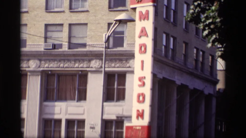 1969 Wisconsin home-movie view of the Madison sign, streetlamp, building windows, and leafy tree cover.