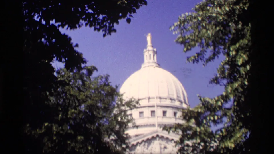 1969 Wisconsin 8mm frame showing a white domed landmark partially framed by leafy trees and blue sky.