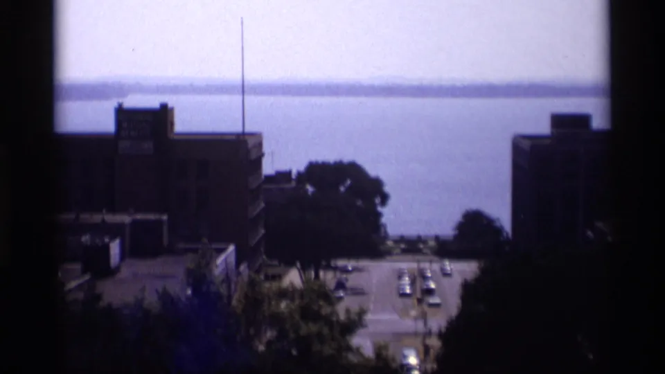 Elevated 1969 view from the Wisconsin Capitol area toward city buildings, cars on a road, and distant water.