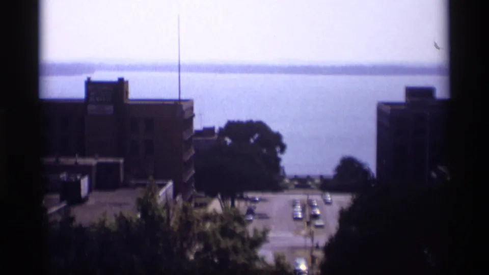 1969 Wisconsin rooftop view looking down a city street toward open water, framed by brick buildings and trees.