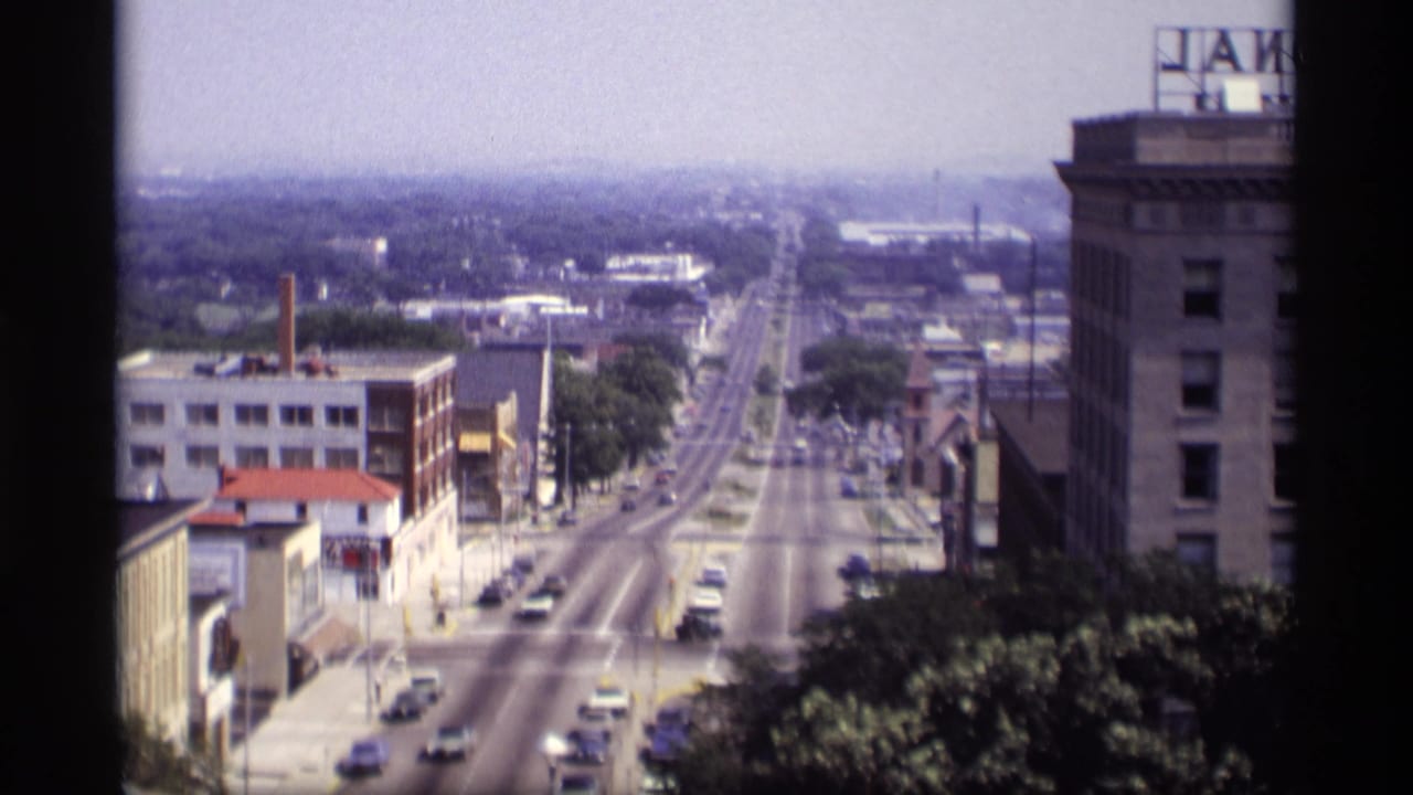 1969 Wisconsin street view from above, showing cars on a broad urban road, mid-century buildings, trees, and partial rooftop signage.