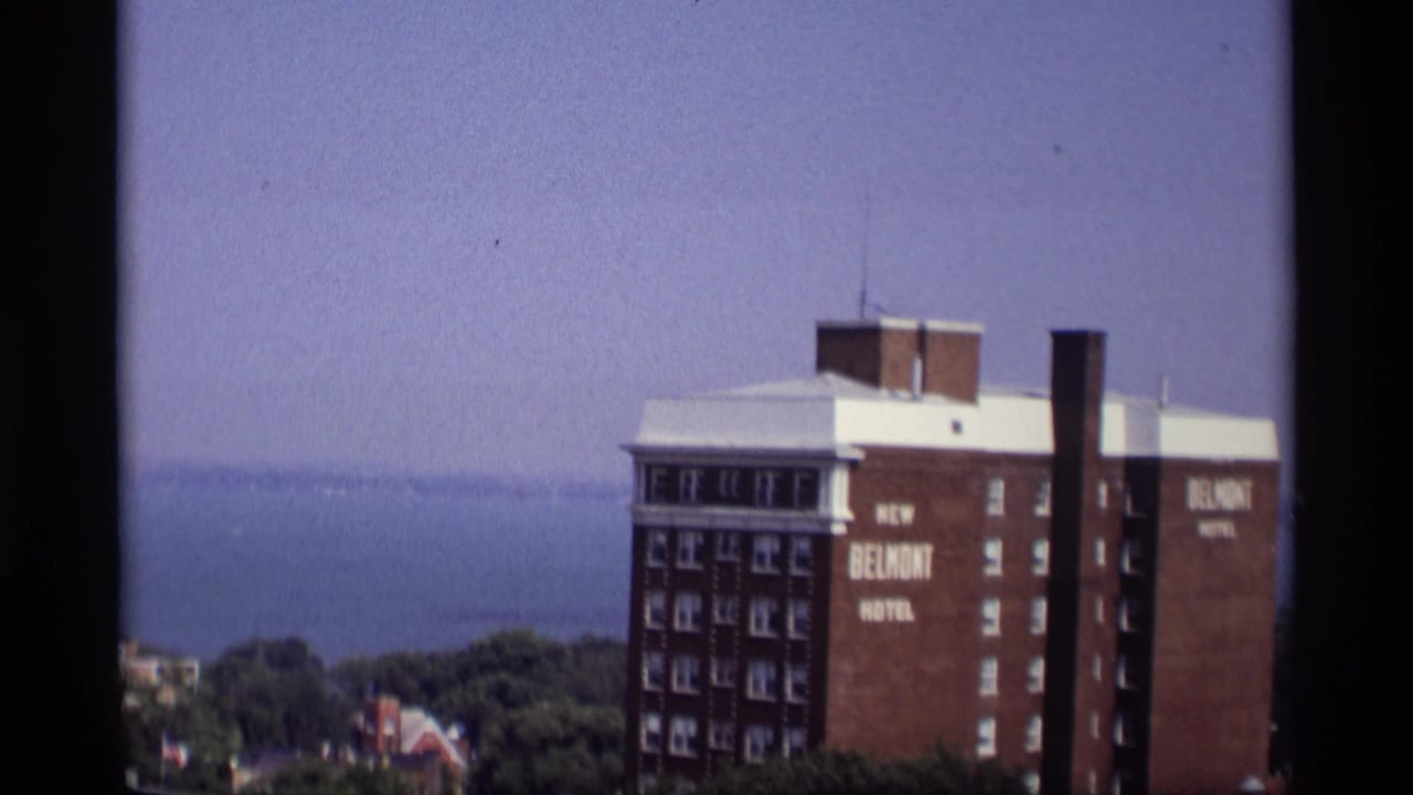 Brick New Belmont Hotel above trees with blue water in the background.