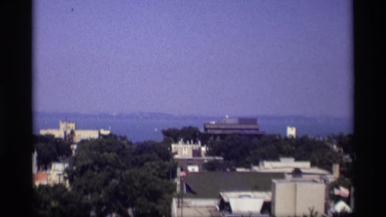 1969 Wisconsin home-movie frame showing an elevated view over trees and rooftops toward distant water.