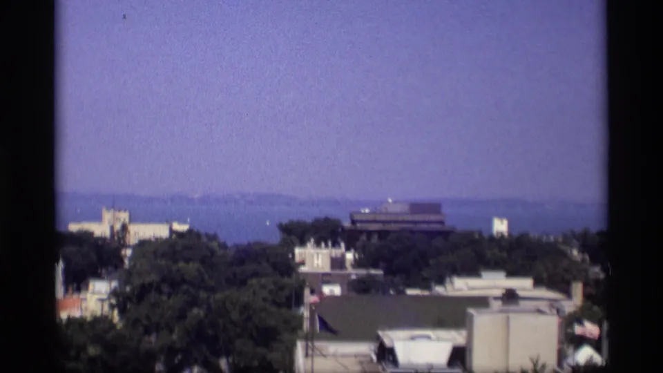 1969 Wisconsin home-movie frame showing an elevated view over trees and rooftops toward distant water.