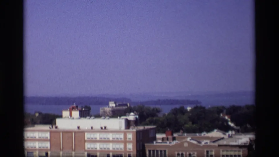 1969 Wisconsin elevated view showing a brick institutional-looking building, trees, and distant water under a hazy sky.