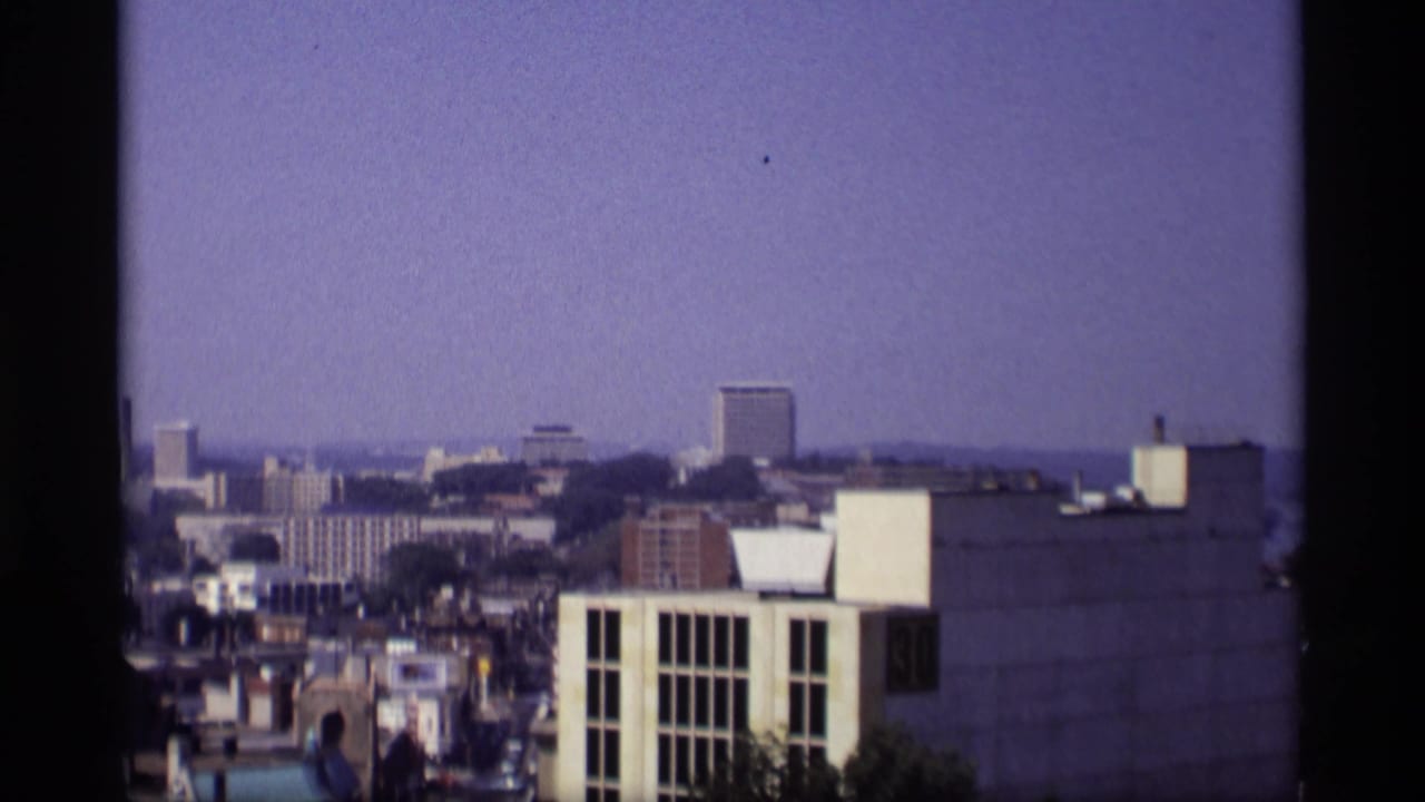 Elevated city skyline with office buildings, rooftops, and a purple-blue sky.