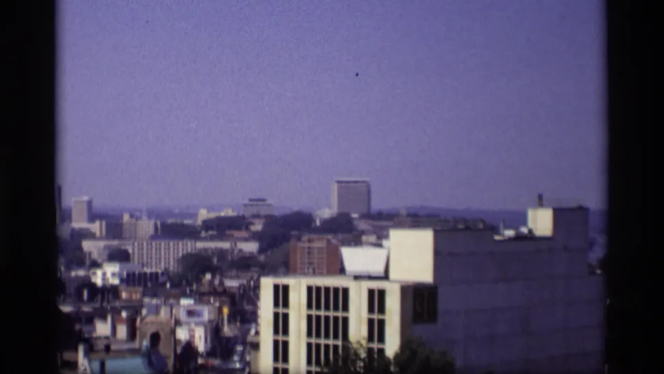 1969 Wisconsin home-movie view over a city skyline with mid-rise buildings, rooftops, and distant haze.