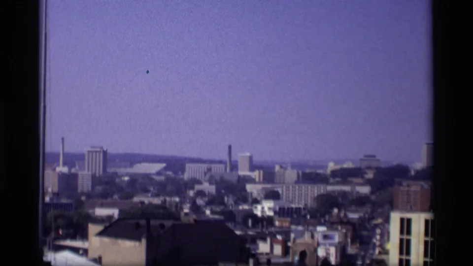 1969 Wisconsin panoramic city view showing rooftops, distant blocks, a smokestack, and hazy sky.