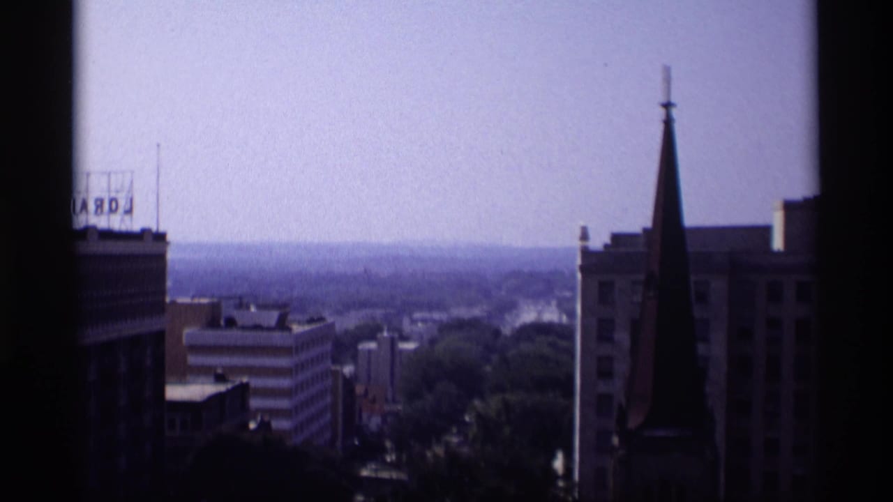 Elevated city view with church steeple, rooftop sign, hazy sky, and dark window framing.
