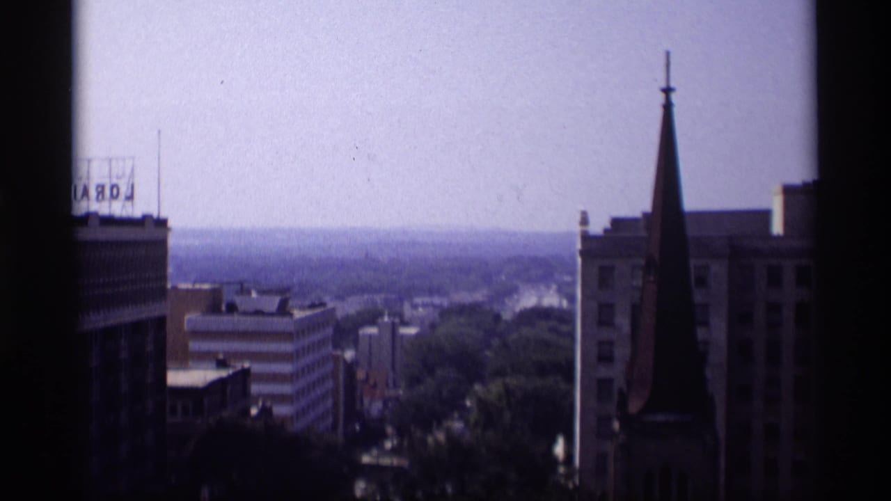 Similar elevated skyline view with steeple, rooftop sign, low buildings, and hazy horizon.