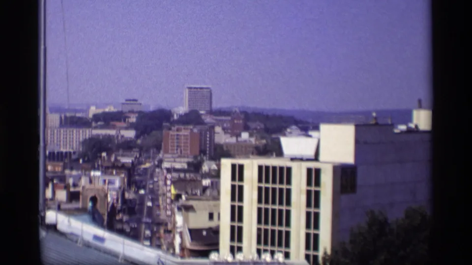 1969 Wisconsin home-movie frame showing downtown blocks, a white foreground building, distant mid-rises, and hazy sky.