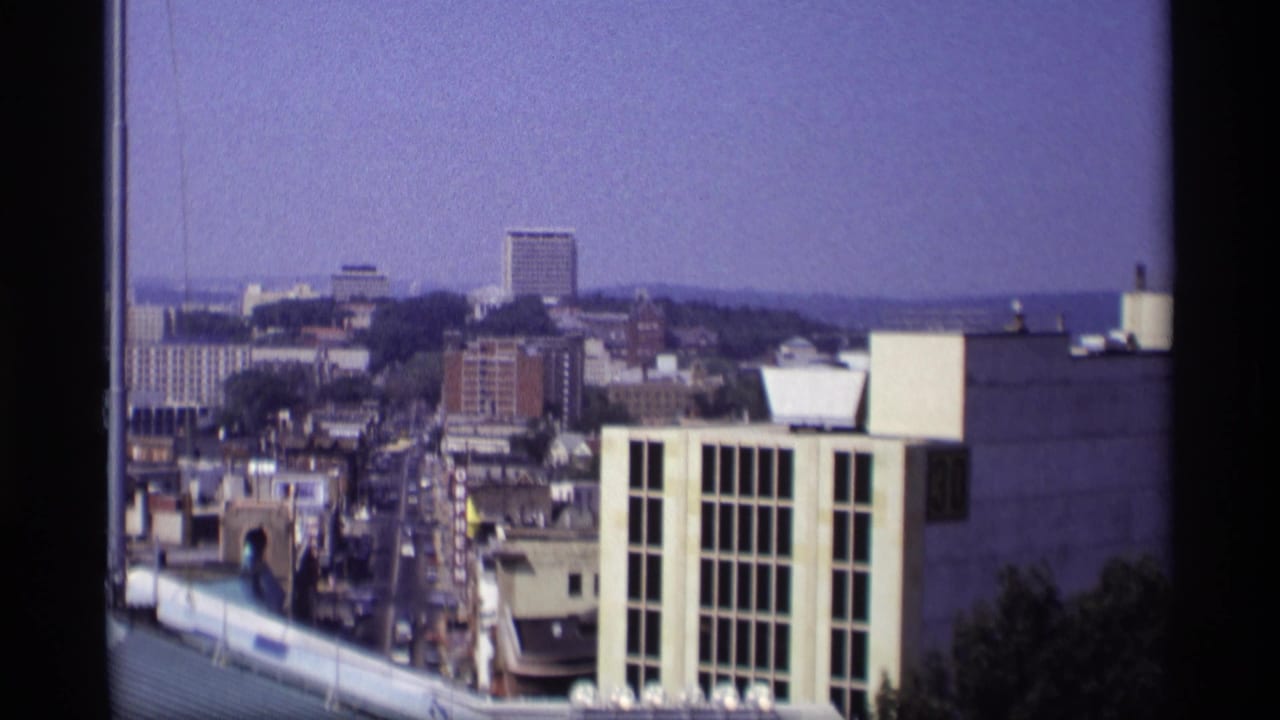1969 8mm view from above a Wisconsin city, showing downtown streets, mid-century buildings, rooftops, and a hazy skyline.