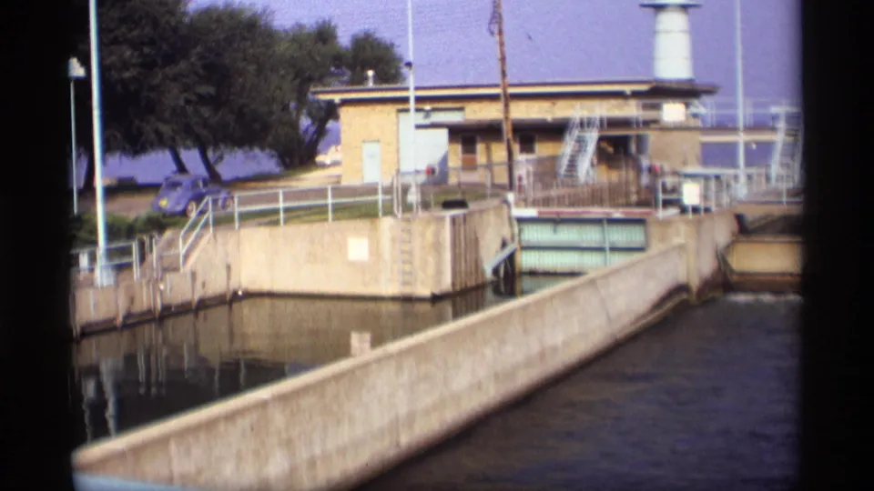 1969 Wisconsin waterway infrastructure showing a concrete lock or dam channel, railings, a small utility building, trees, and a blue car.