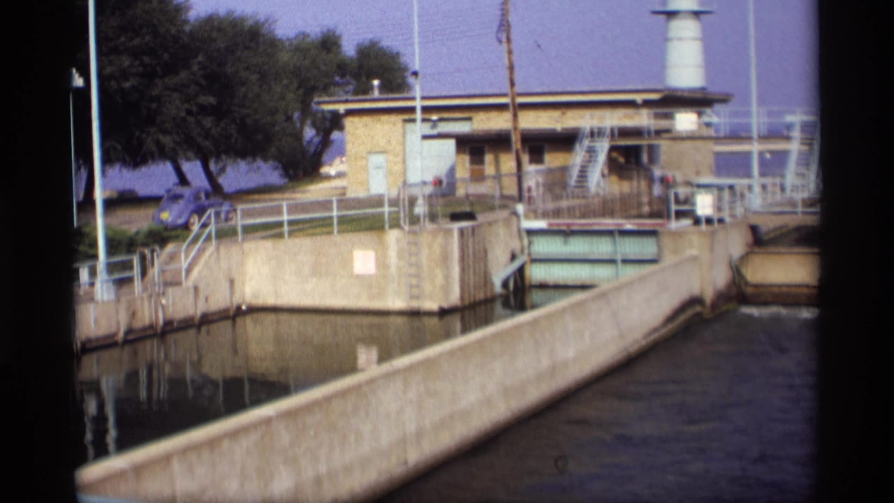 Concrete canal leading toward a brick water control building with railings and a white tower.