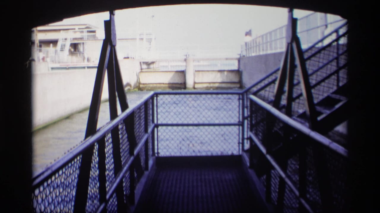 1969 Wisconsin 8mm frame showing a metal walkway, stairs, chain-link railings, and a concrete canal with water beyond.