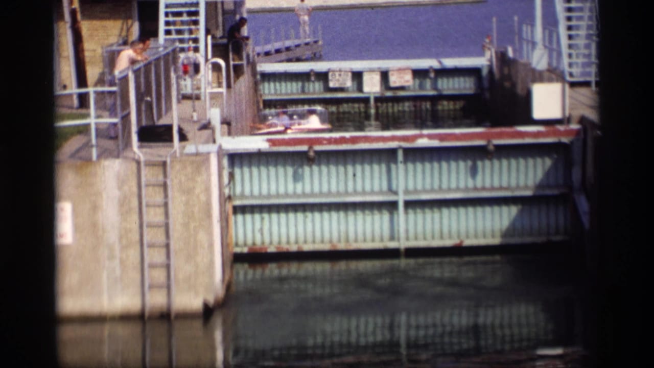 Metal canal lock gate and concrete walkway with people standing near railings.