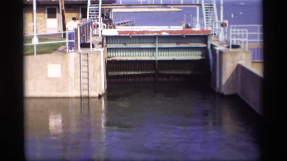 The Wisconsin drawbridge is partly open, with the wheel-like mechanism visible below the lifting gate and two people nearby.