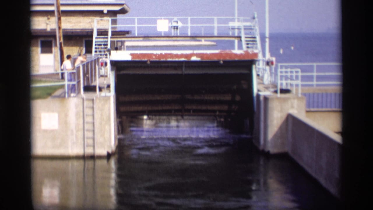 Canal lock entrance with concrete walls, railings, water, and two people standing near the left side.