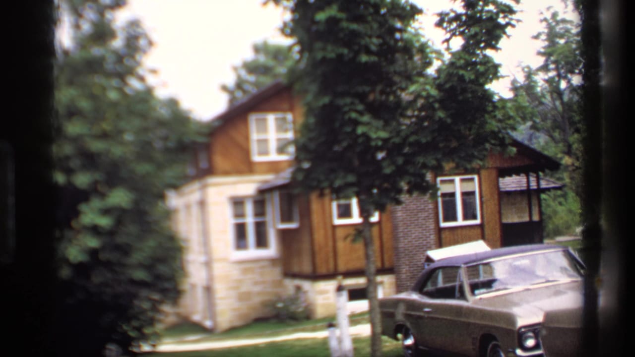 Similar view of a wooded house and parked sedan, framed through dark film edges.