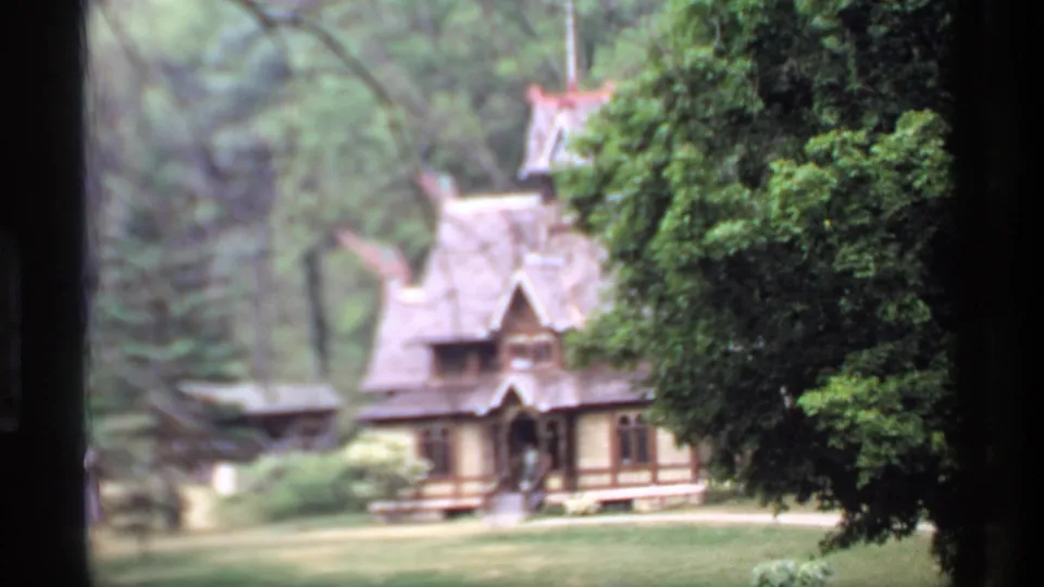 1969 Wisconsin home-movie frame of a large rustic wooden house with steep gables, lawn, and trees, partly seen through a dark frame.