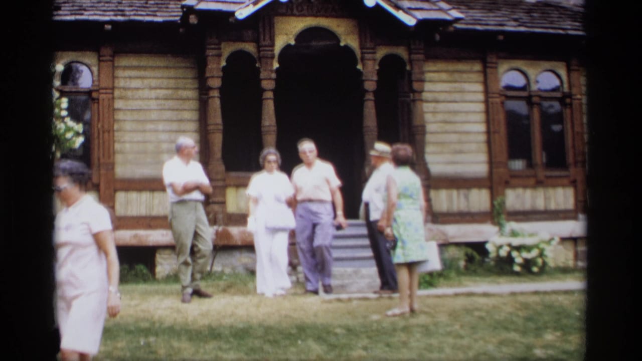 Adults gather near the steps of an ornate wooden building with arched porch openings.