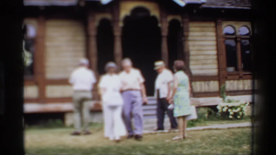 Adults approach and stand near the steps of the ornate wooden building during a 1969 Wisconsin tourist stop.
