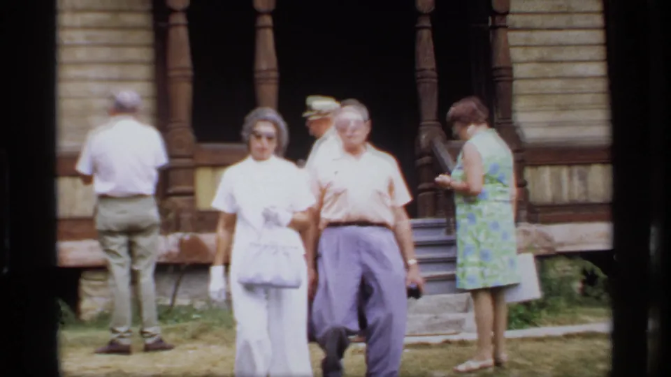 Two visitors walk toward the camera as others stand by the dark arched porch of the Wisconsin wooden building in 1969.