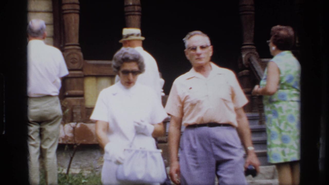 Adults walking in front of an older house with a covered porch and wooden posts.