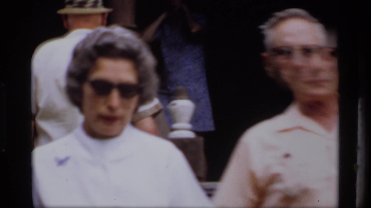 Close view of a woman in sunglasses and a man walking near a porch entrance.