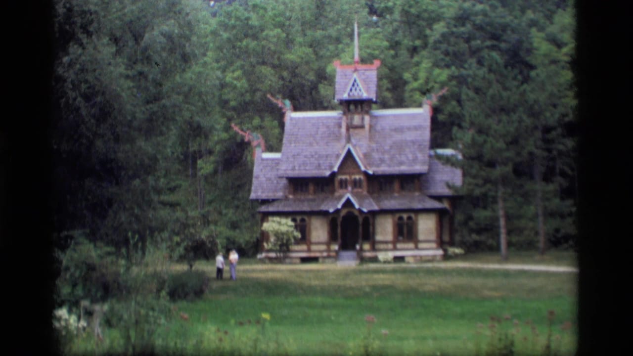 Decorative wooden building in a forest clearing with two distant visitors on the lawn.