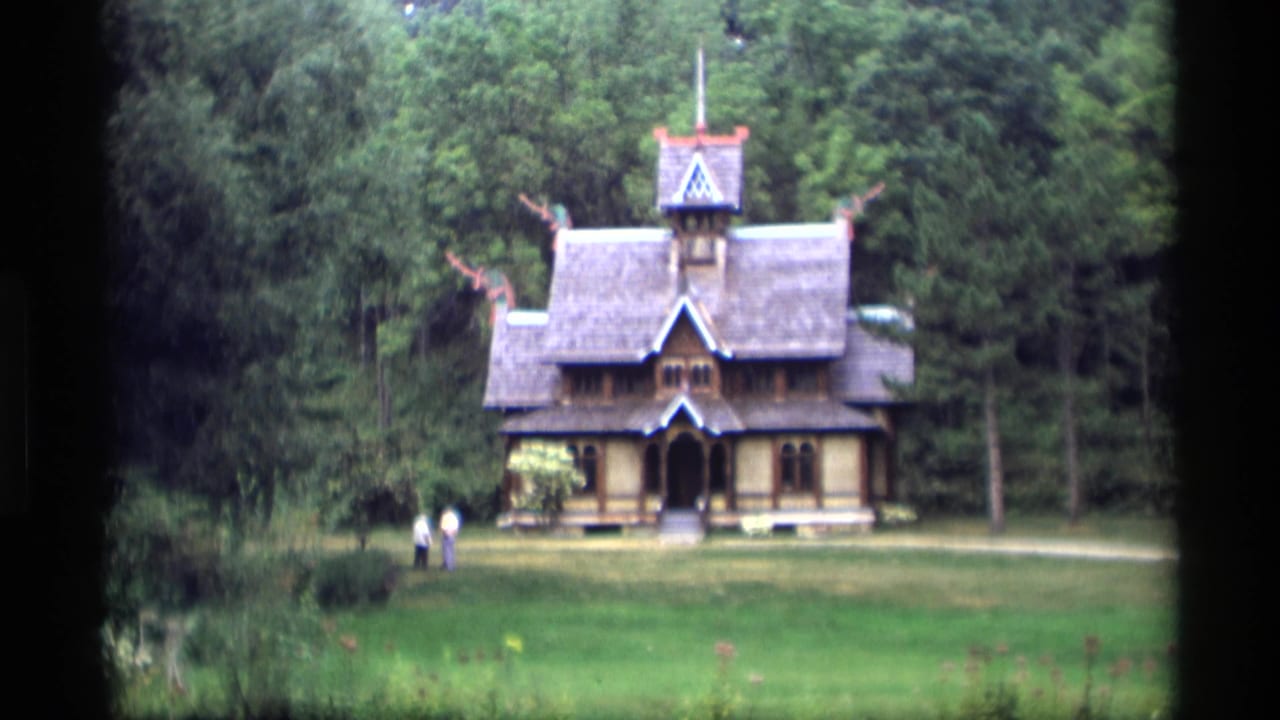 Wooded landmark building centered beyond a grassy lawn with two people nearby.