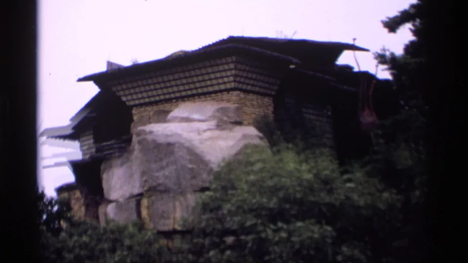 1969 Wisconsin 8mm frame showing a rustic exterior with stone base, wood wall texture, dark roof, and surrounding trees.